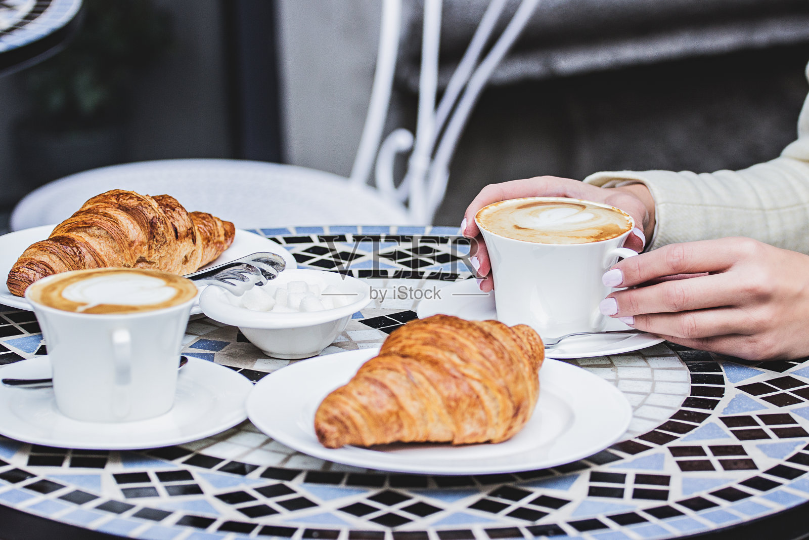 女人手持咖啡杯的侧视图，复古桌上的羊角面包和咖啡照片摄影图片