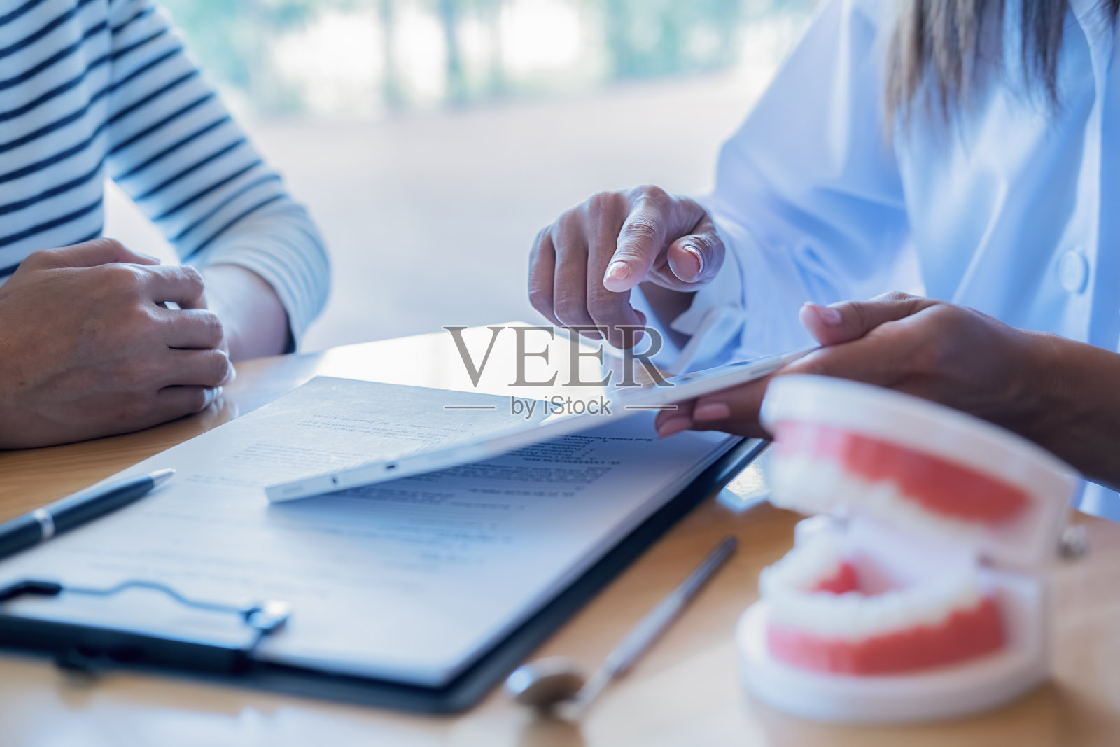 牙医在牙科诊所使用牙齿模型和探针镜向患者讲解牙齿疾病的治疗方法，医疗保健概念照片摄影图片