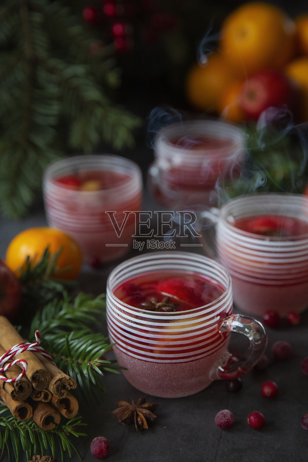 冬天热饮料。圣诞餐桌上放着热红酒、橘子、橘子、苹果、圣诞树和蔓越莓。照片摄影图片