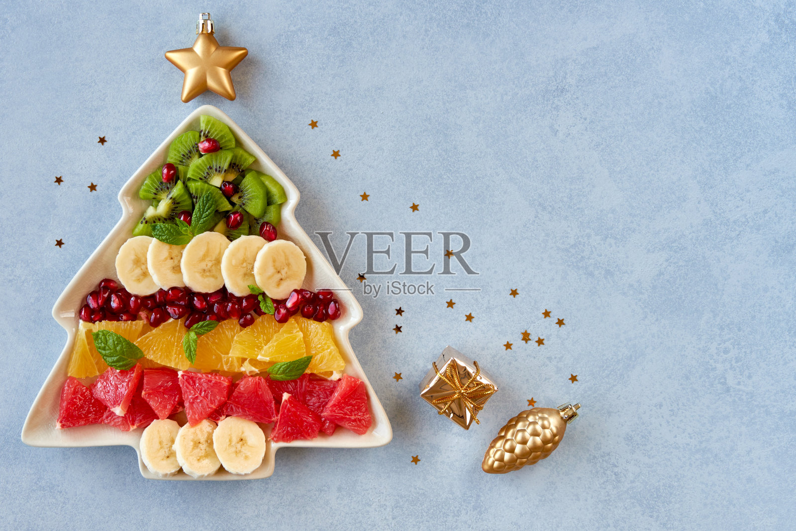 圣诞背景与水果沙拉在冷杉树形状的盘子和节日装饰。俯视图平铺照片摄影图片