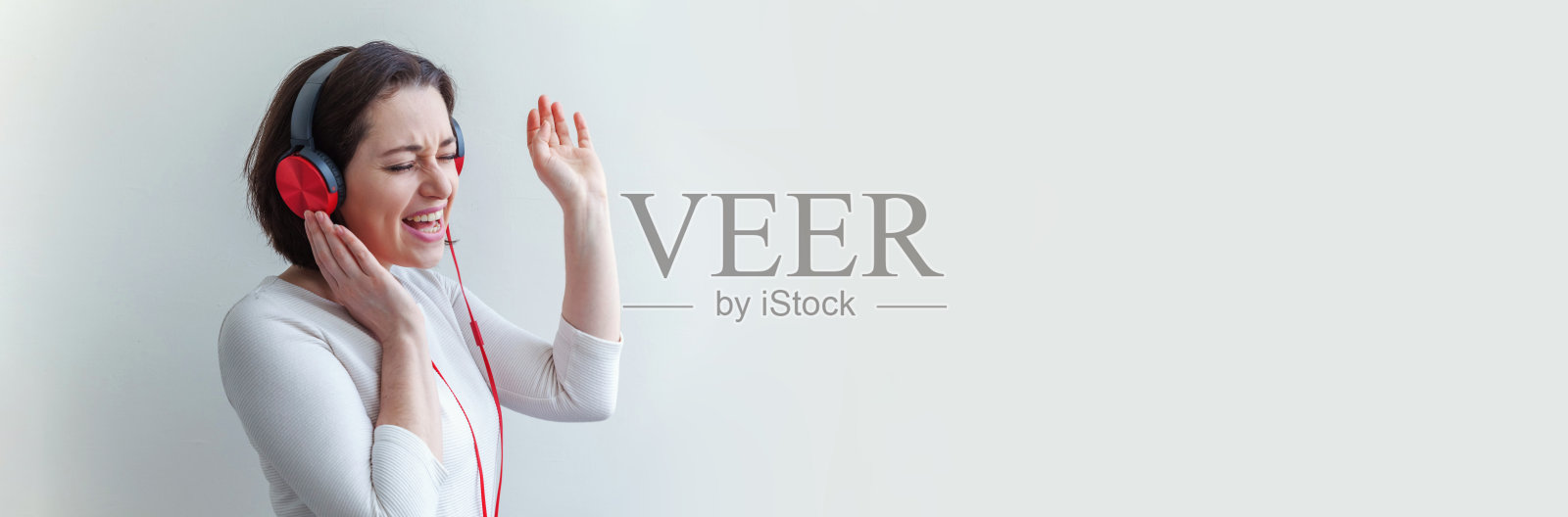 戴着耳机唱歌的年轻棕发女子，白色背景banner照片摄影图片