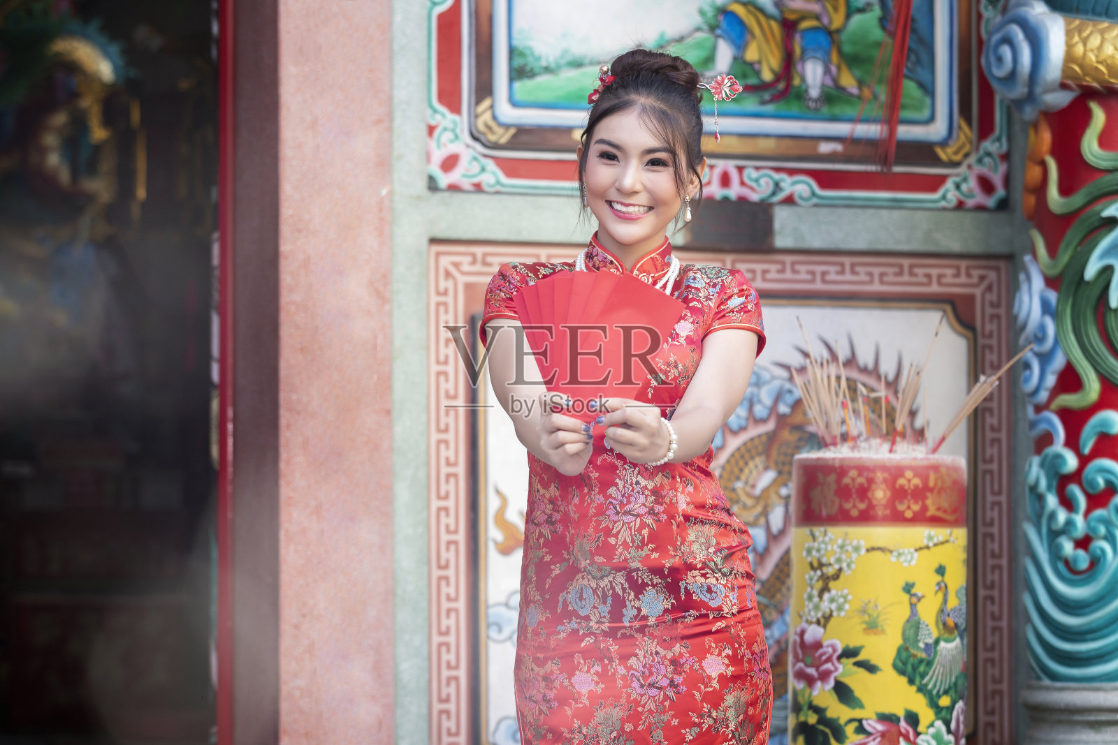 庆祝中国新年的概念:身着红色旗袍的中国妇女拿着红包在神祠。照片摄影图片