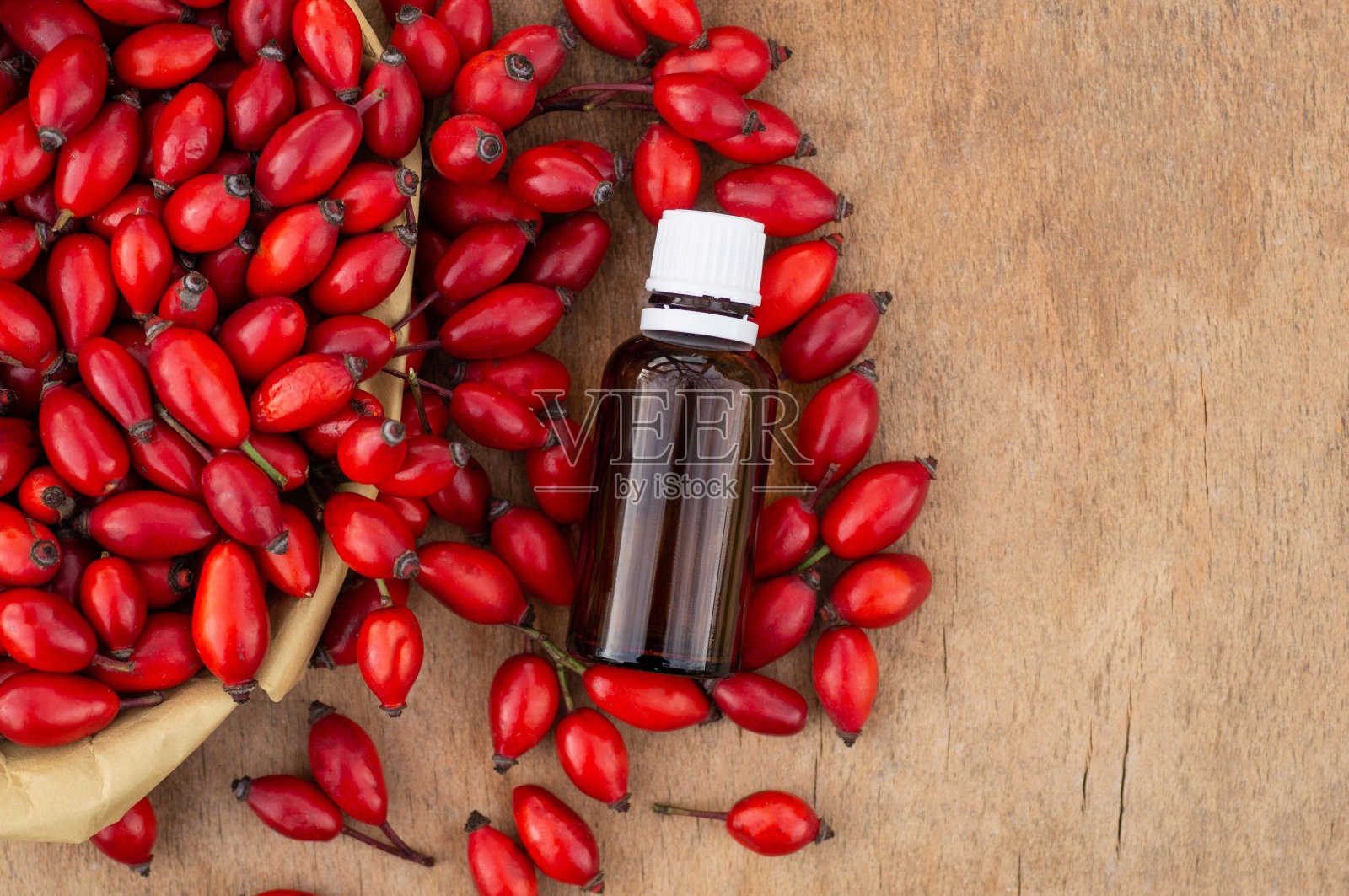 木桌上放着玫瑰果和玫瑰果籽油。蔷薇果，俗称蔷薇果(Rosa canina)照片摄影图片