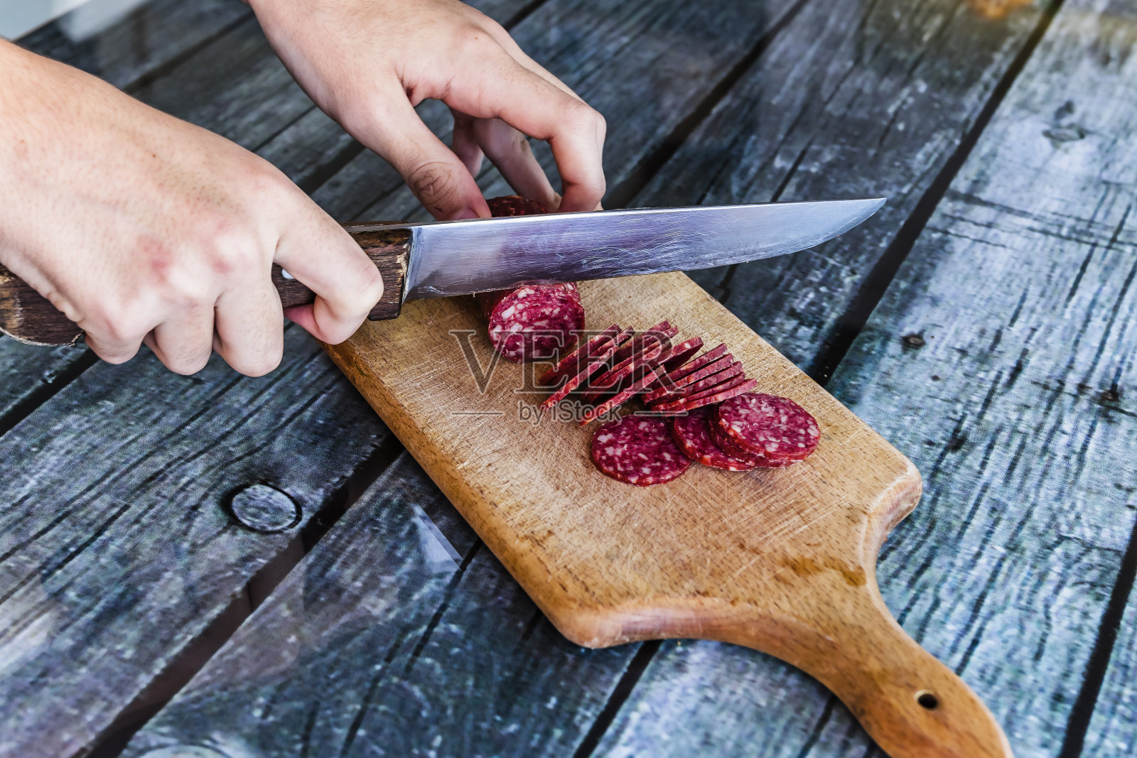 男人用刀切割萨拉米香肠照片摄影图片