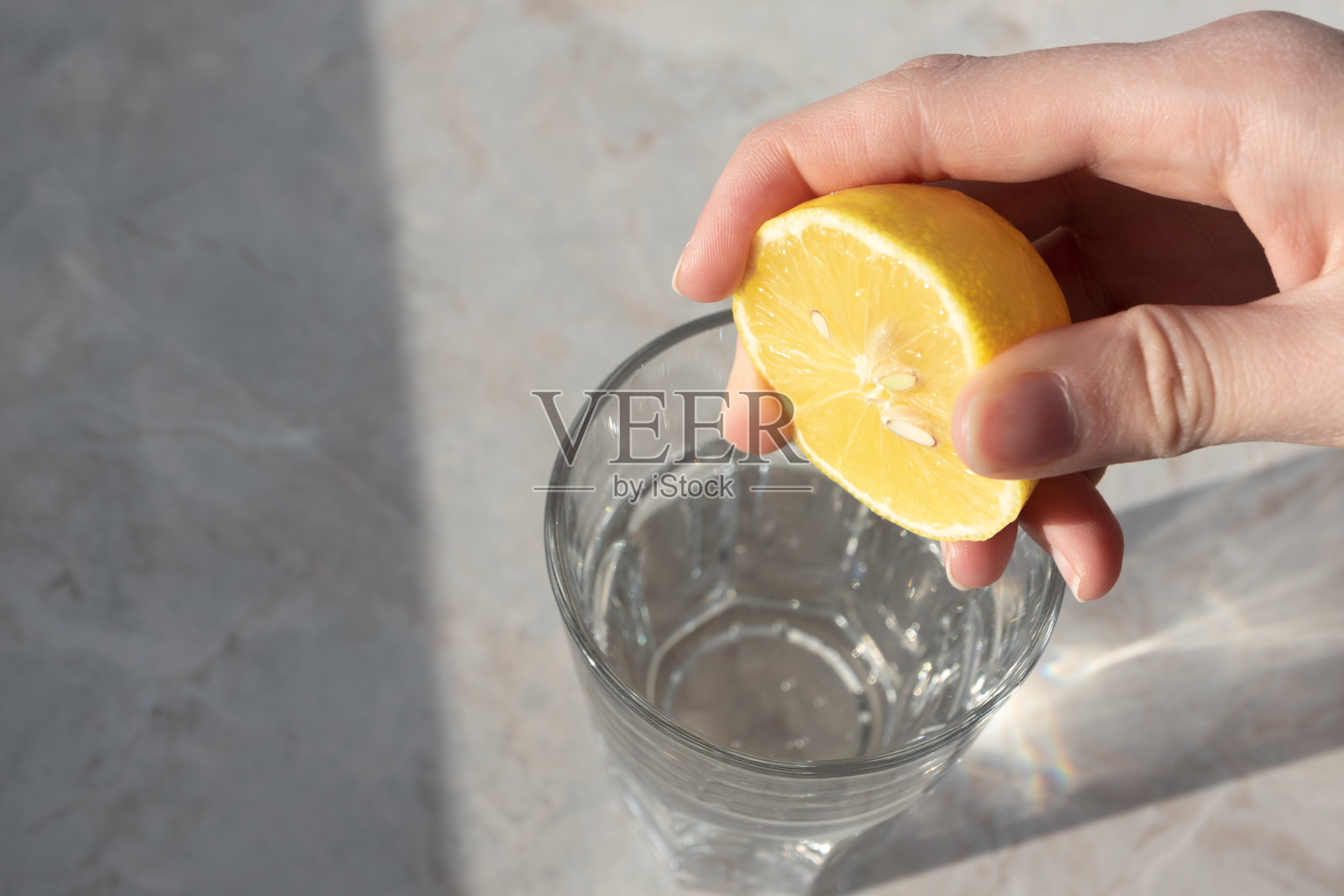 女人在装有苏打水的玻璃杯中挤柠檬汁，健康排毒饮品照片摄影图片