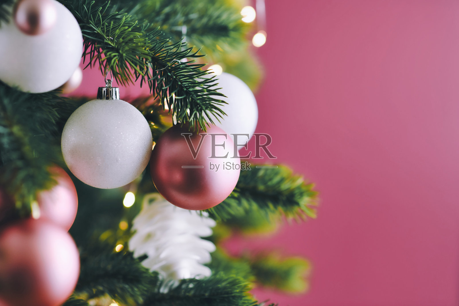 近距离装饰圣诞树与白色的季节性和粉红色的树饰品，如小饰物和星星在暗粉色的背景与灯的背景照片摄影图片