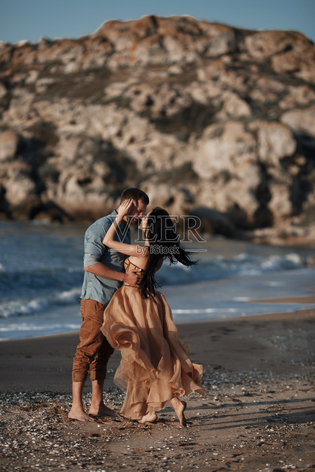 一对幸福的情侣在蓝色海洋附近的岩石海滩度蜜月照片摄影图片