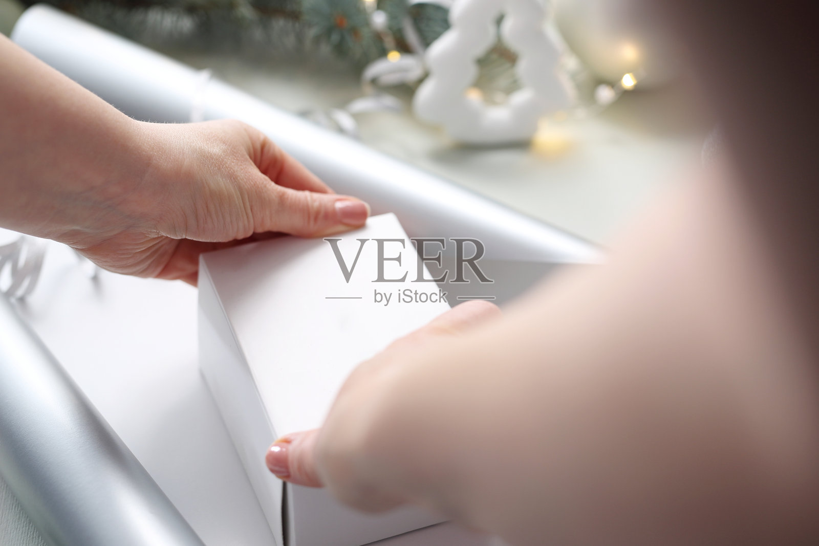 节日礼物。在圣诞树下，一位妇女用银纸包着礼物。照片摄影图片