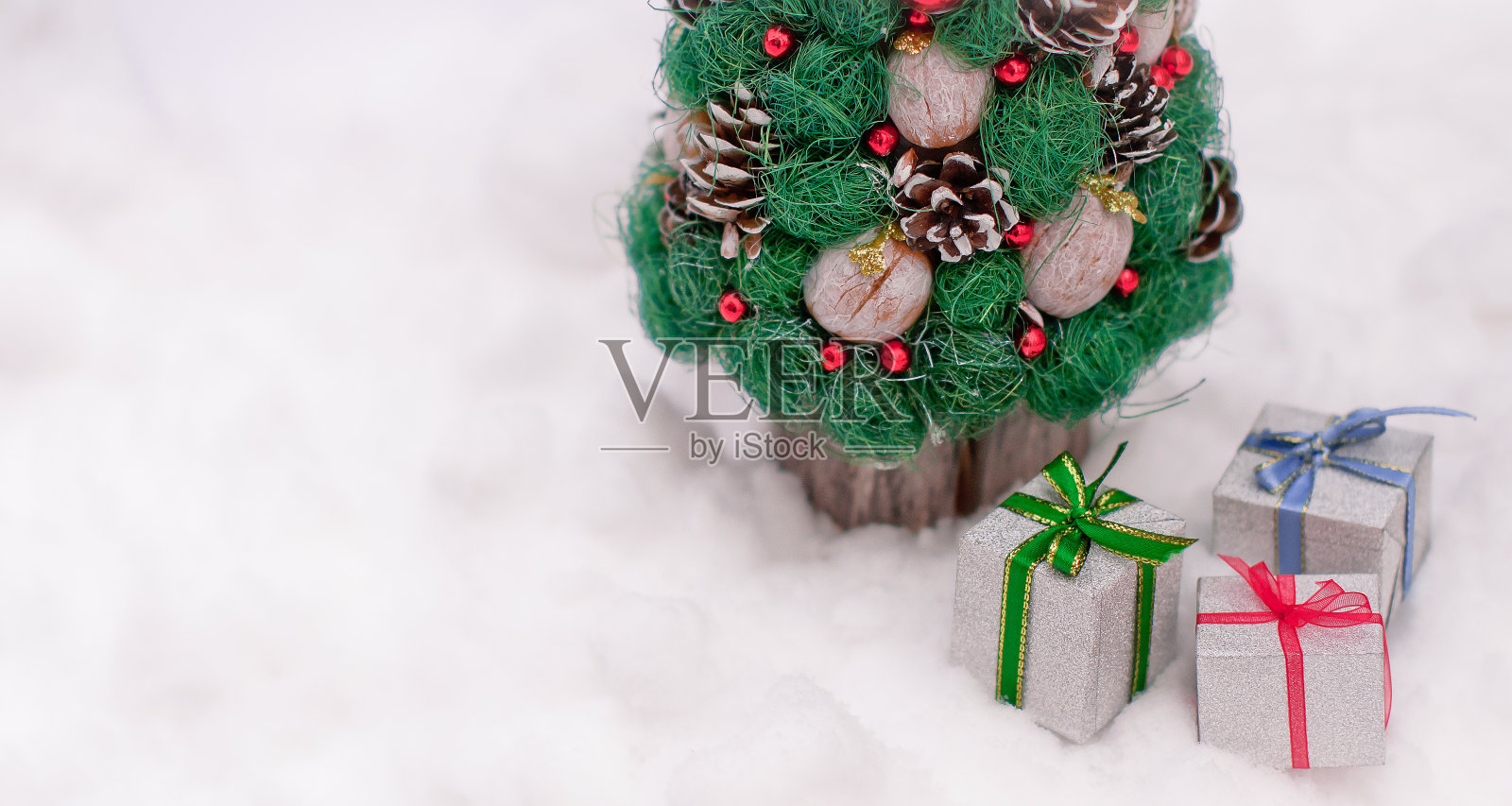 新年礼物包装闪亮，彩带鲜艳，躺在街上的雪堆里，在一棵绿色的圣诞装饰树下，有锥形的锥体和装饰，有文字的地方照片摄影图片