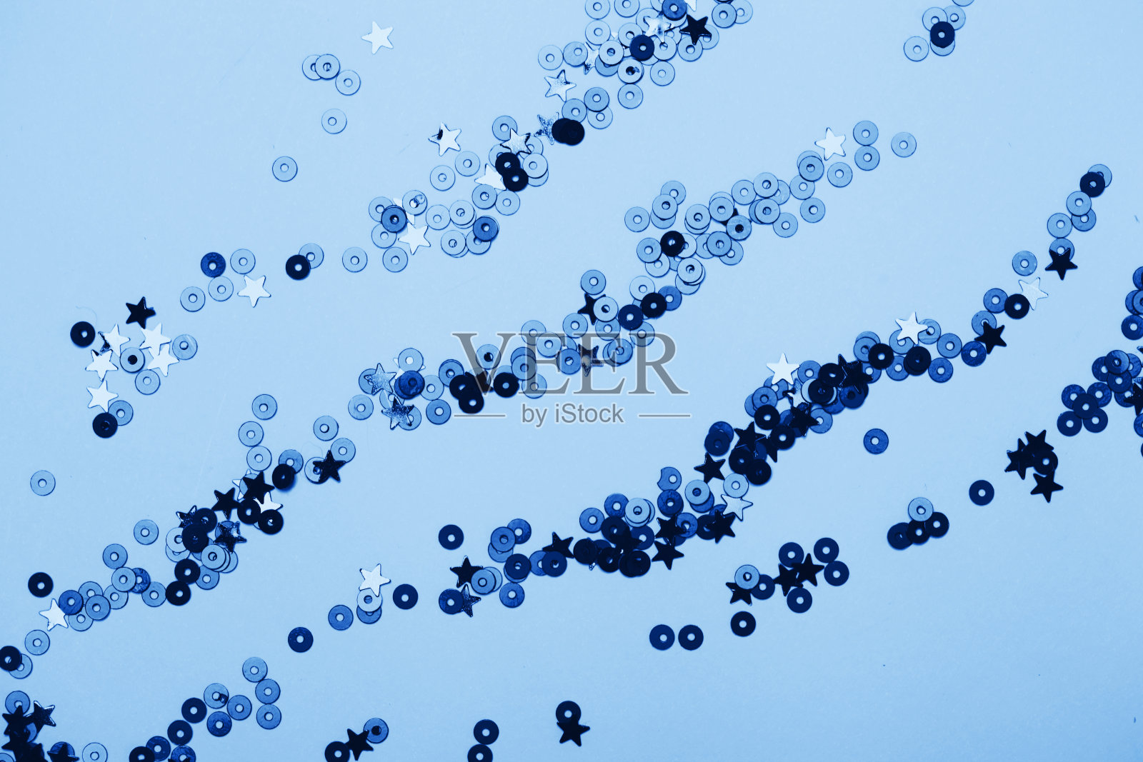 蓝色背景上点缀着经典的蓝色五彩纸屑和星星。照片摄影图片