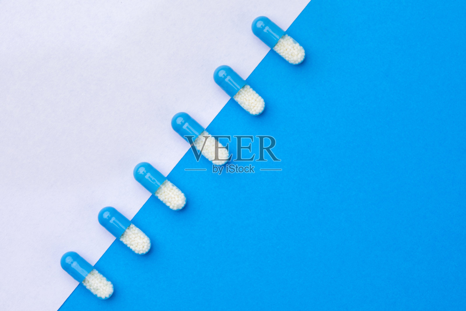 蓝色和白色背景上排列的一排药丸。药房药品的背景。照片摄影图片