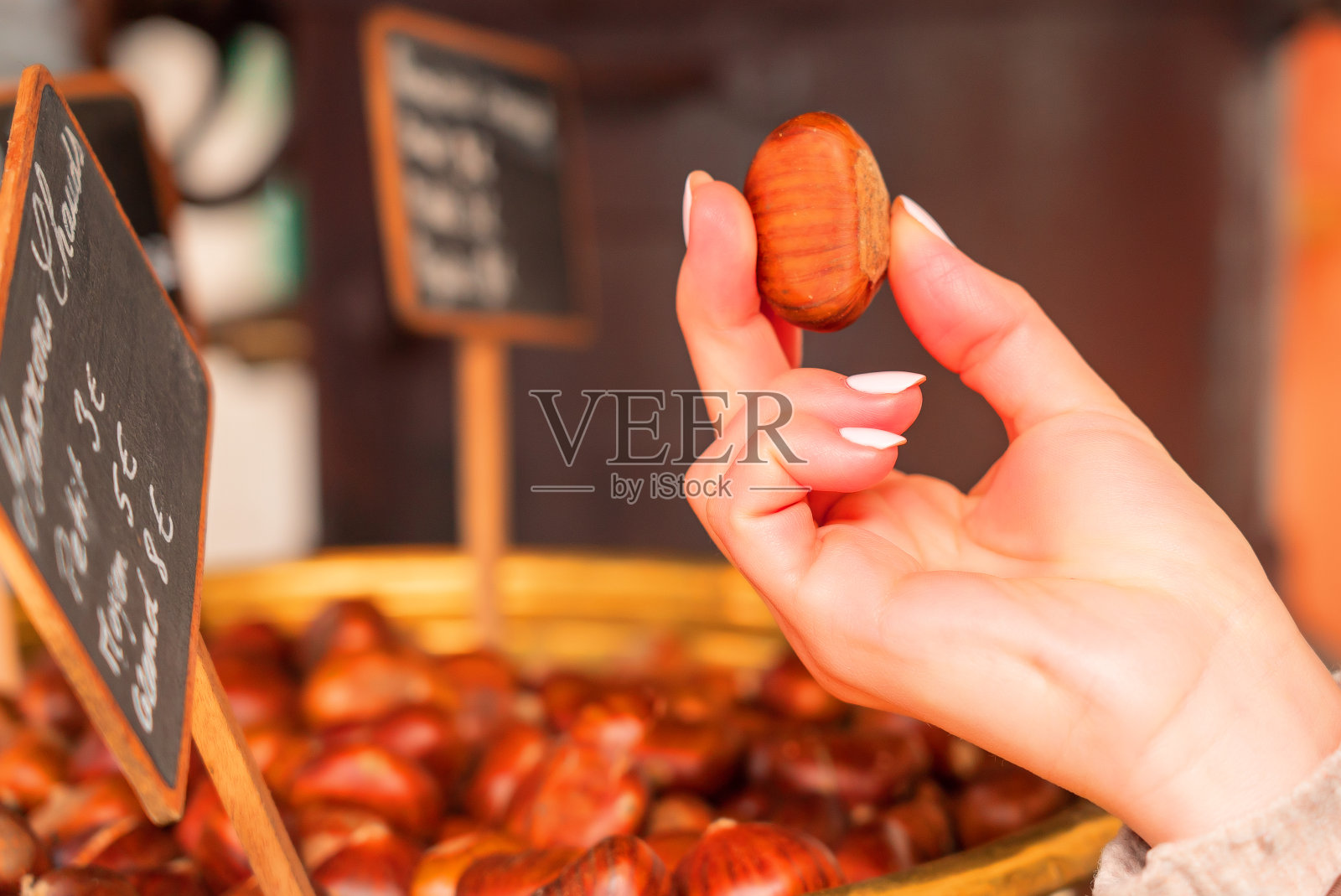 女人手里拿着烤栗子。巴黎蒙马特的铜制碗，上面有栗子和价格标签。照片摄影图片