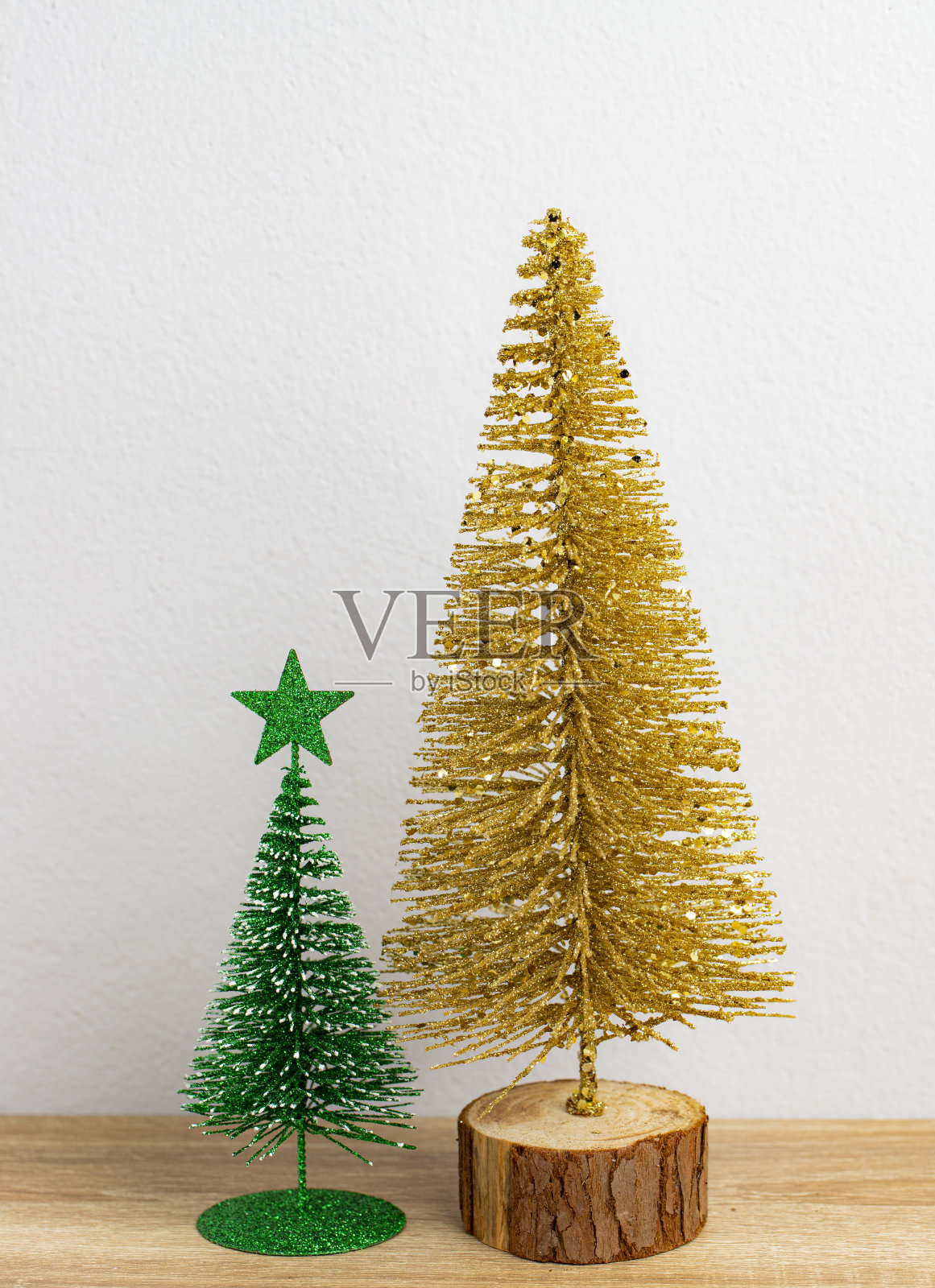 金色的圣诞树和绿色的小圣诞树放在棕色的桌子和白色的背景上照片摄影图片