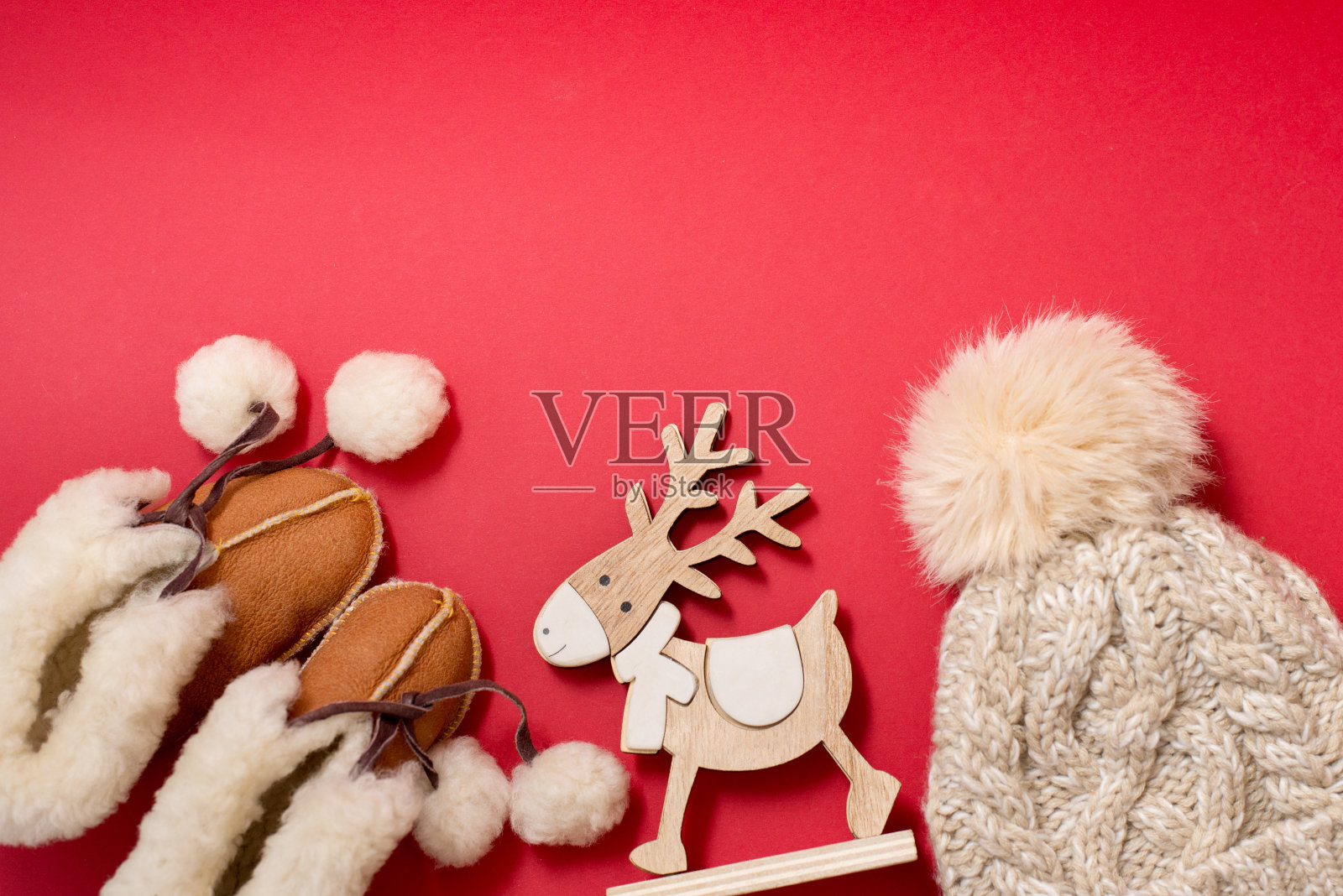 婴儿冬季衣服靴子和帽子上的红色背景与木制玩具鹿，复制空间照片摄影图片