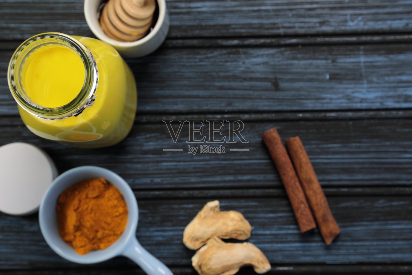 姜黄拿铁、黄金牛奶或含有超级食物姜黄粉、姜粉和肉桂的印度抗炎Doodh，在木质背景下用蜂蜜加糖照片摄影图片