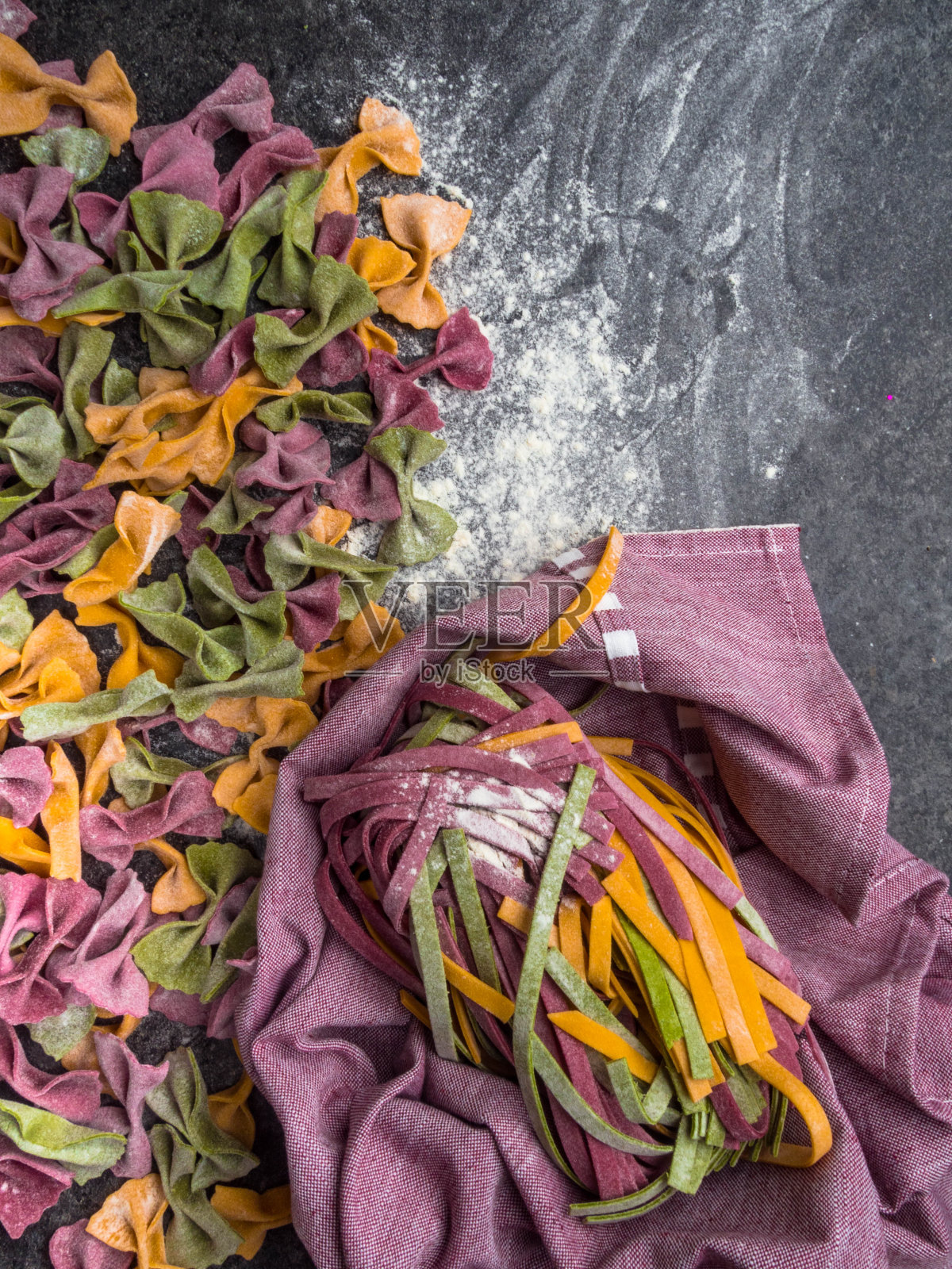 各种生意大利面类型，法falle领结，宽面条或宽面条彩色意大利面在灰色背景与面粉照片摄影图片