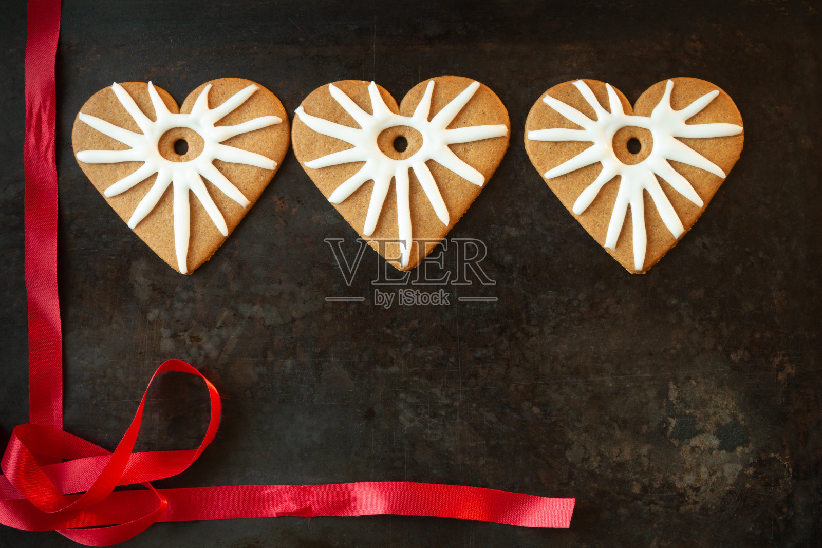 三个姜饼心型的饼干，黑色的背景上有红色的丝带照片摄影图片