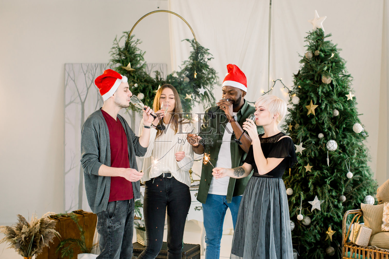 圣诞快乐，恭贺新禧!多种族的富有创造力的年轻人在舒适装饰的工作室庆祝节日。一群年轻人拿着孟加拉火喝着香槟。照片摄影图片