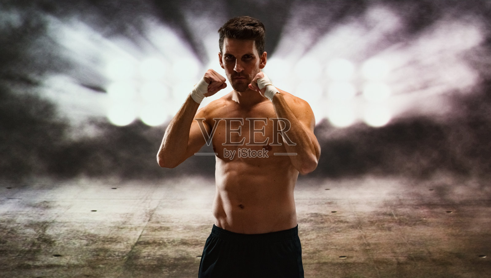 一个男人/一个人/腰部以上/正面30-39岁的成年人英俊的人白人男性/年轻男子锻炼/站在户外穿着跑步短裤/短裤和显示拳头/电灯/晚上/点照明/混凝土照片摄影图片