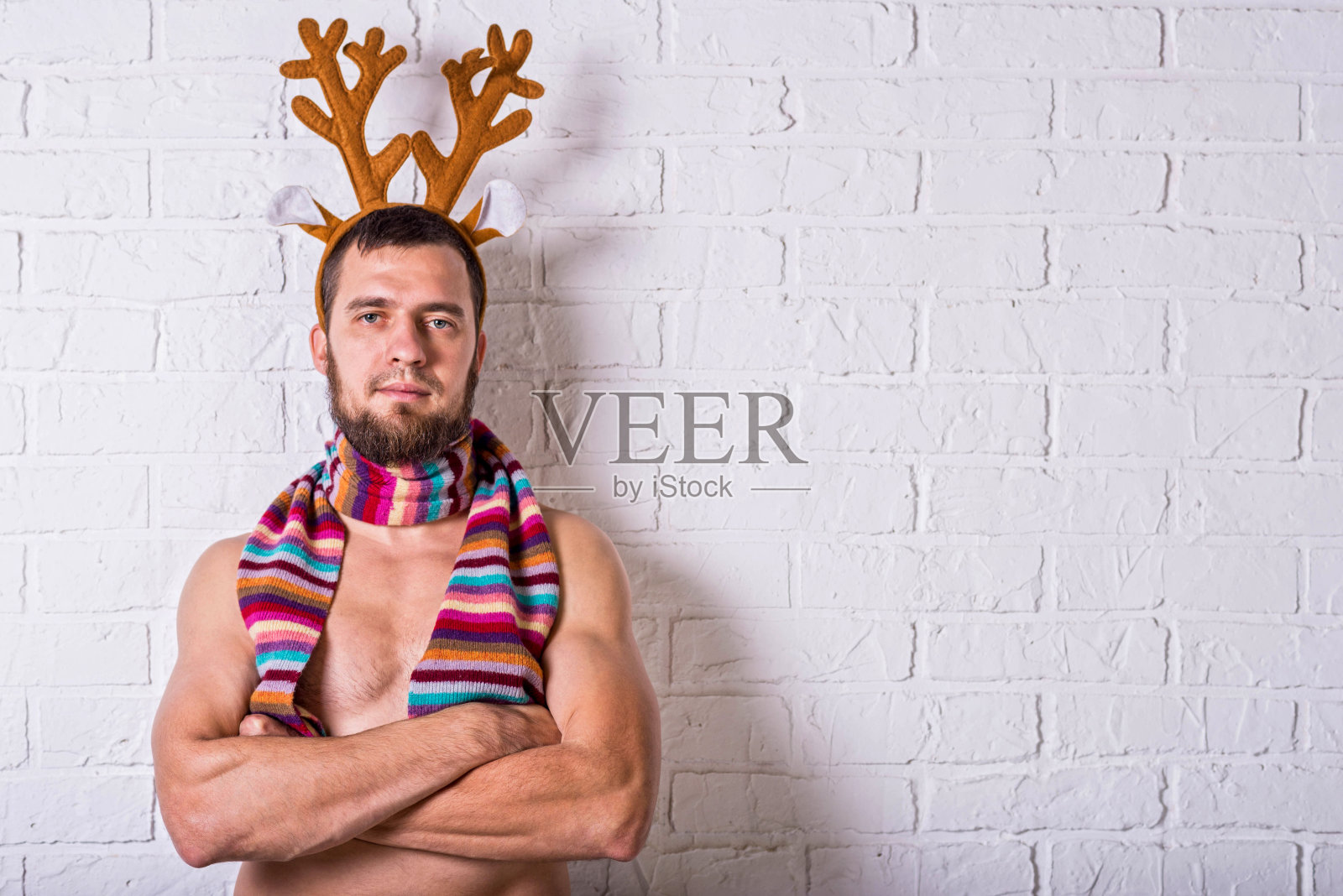 一个愉快和有趣的人的肖像鹿角和条纹围巾上的白砖墙，复制空间。照片摄影图片