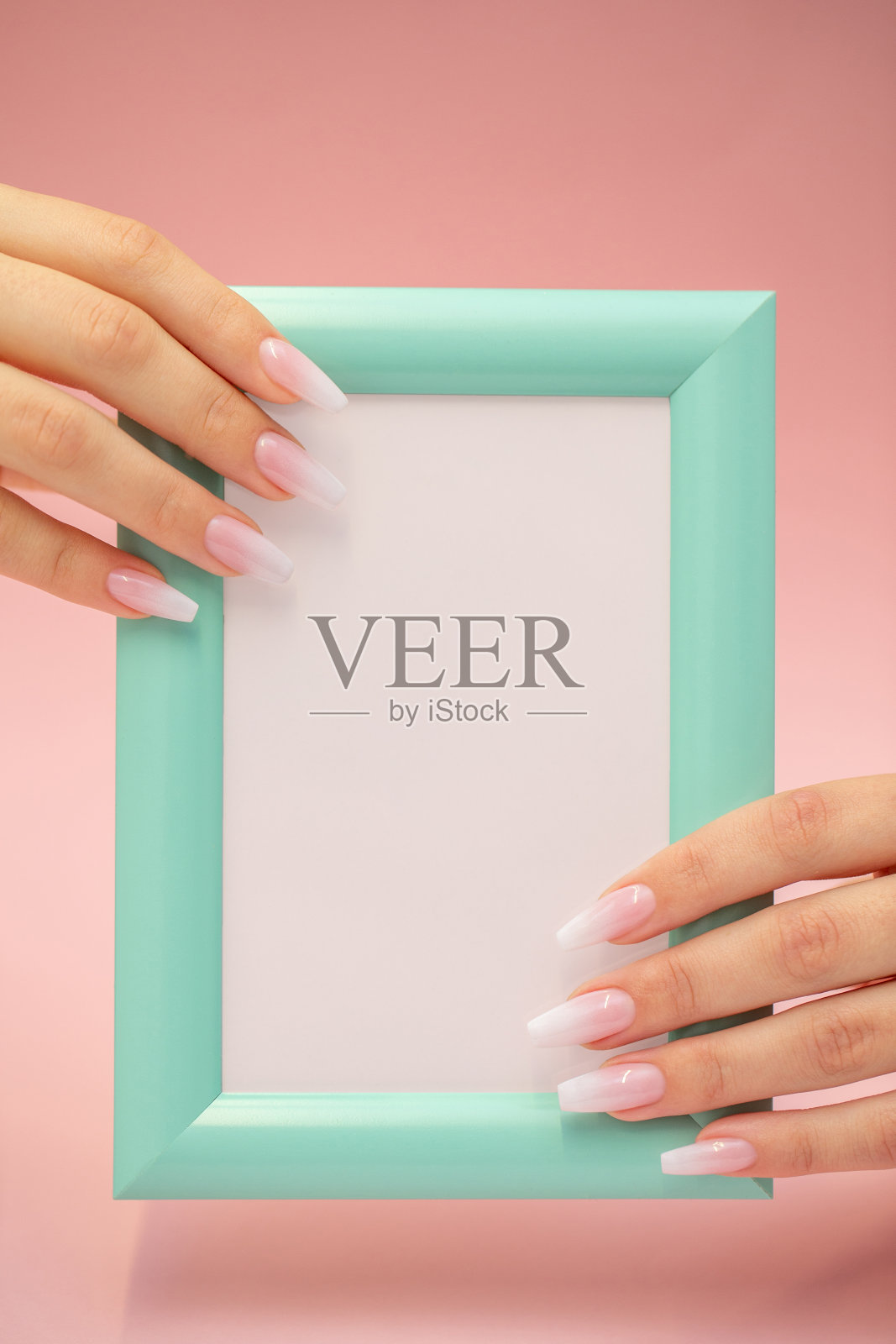 美丽的手指抱着一个小空白Torquiest框架广告对粉红色的背景照片摄影图片