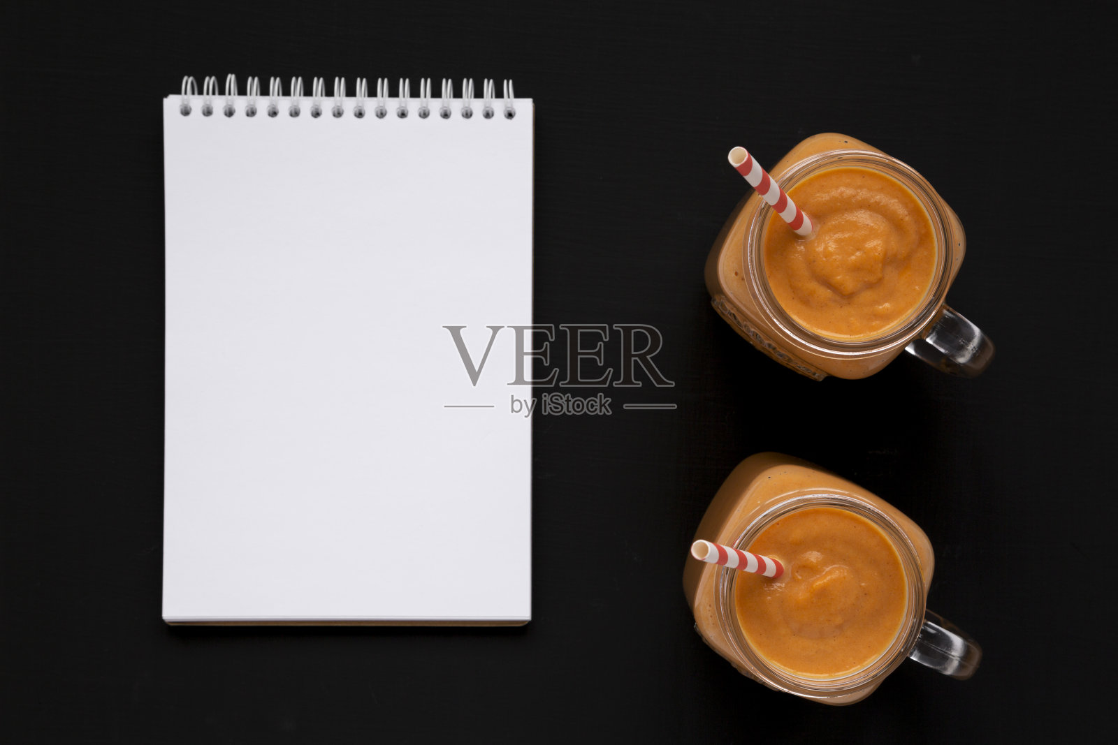 自制的玻璃瓶南瓜奶昔，黑色背景上的空白记事本，俯视图。平躺着，从上面俯视。空间的文本。照片摄影图片