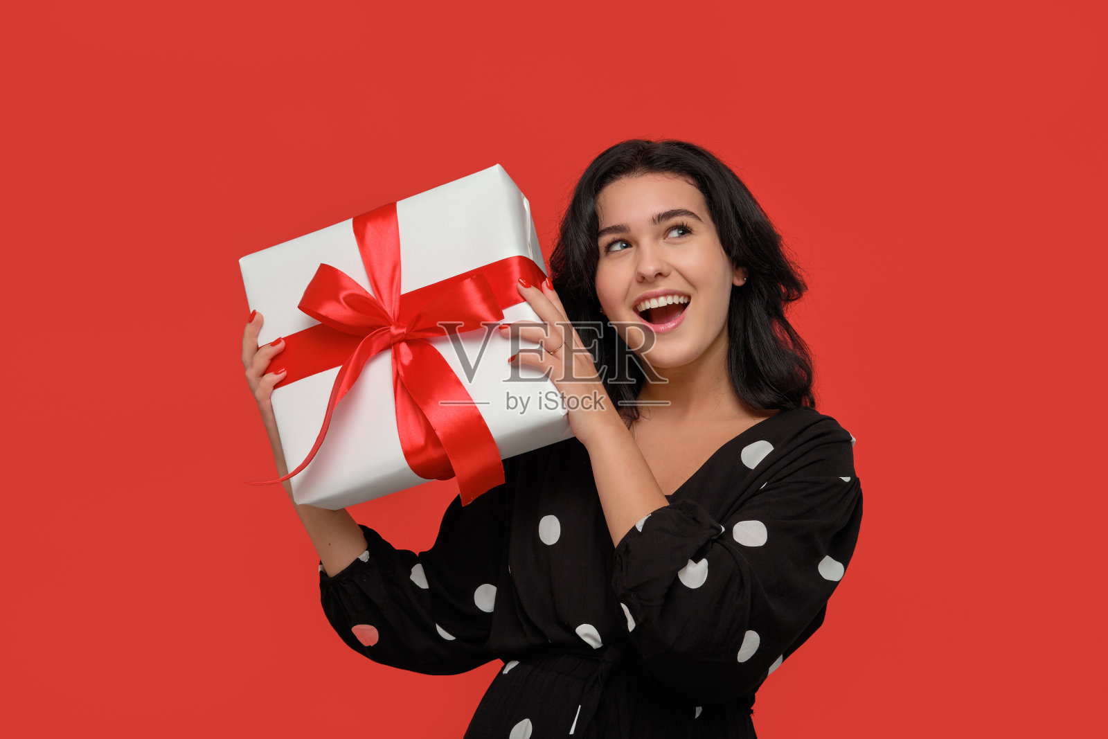 深色头发的女人在一个黑色的裙子微笑着拿着圣诞礼物盒白色与红色的丝带。照片摄影图片