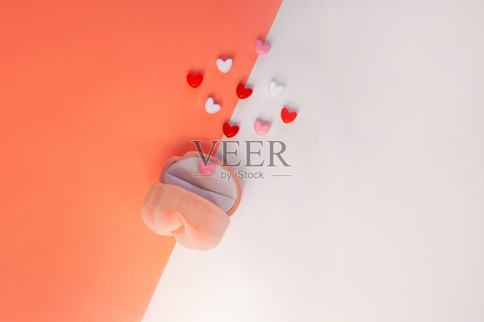 白色和珊瑚橙色背景上的粉色天鹅绒戒指盒，带有心形图案。情人节婚礼求婚珠宝袋照片摄影图片