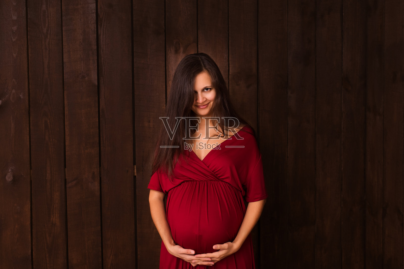 身穿红色连衣裙的孕妇双手搭在深棕色的腹部上。怀孕，母性，期望概念。美丽柔情的怀孕照片照片摄影图片