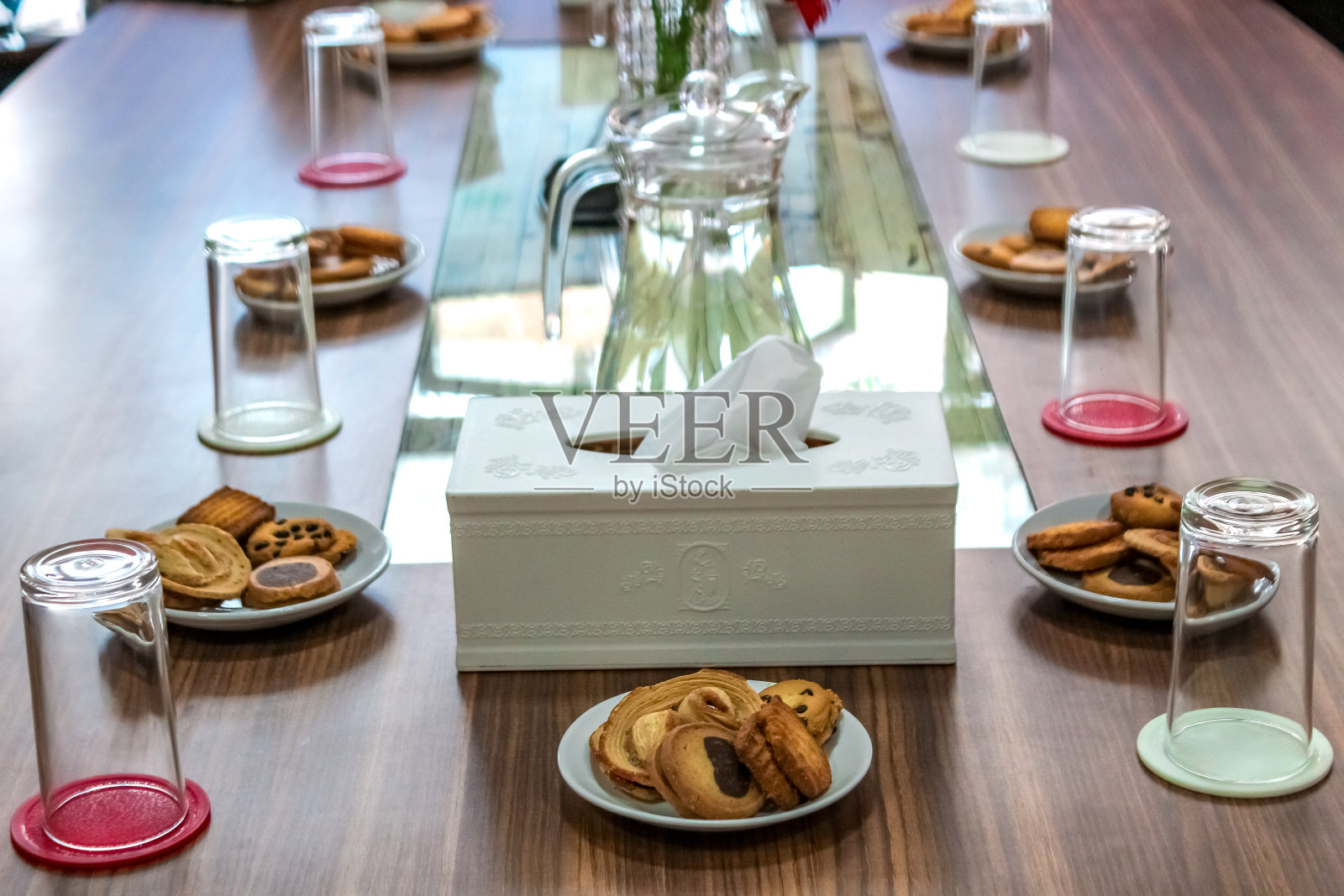 商务人士坐在桌子上开会，木桌上放着饼干、玻璃和一罐水照片摄影图片