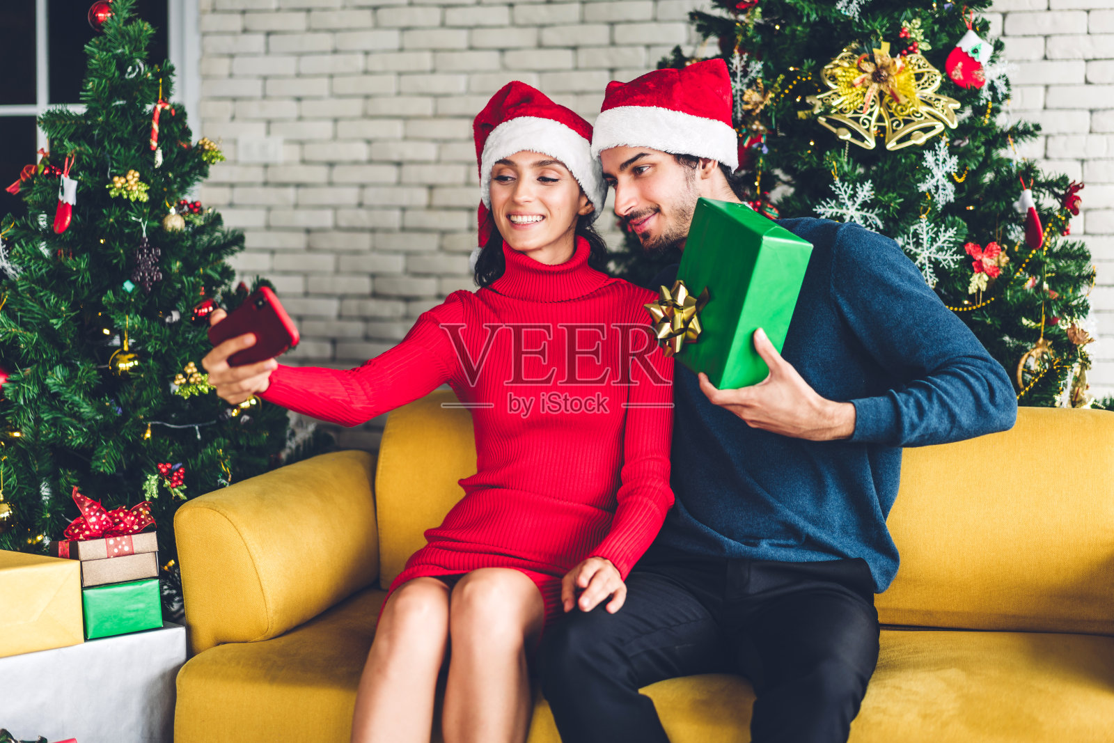 这对浪漫的情侣戴着圣诞帽，微笑着装饰圣诞树，欢度新年。男人给女人惊喜的礼盒照片摄影图片