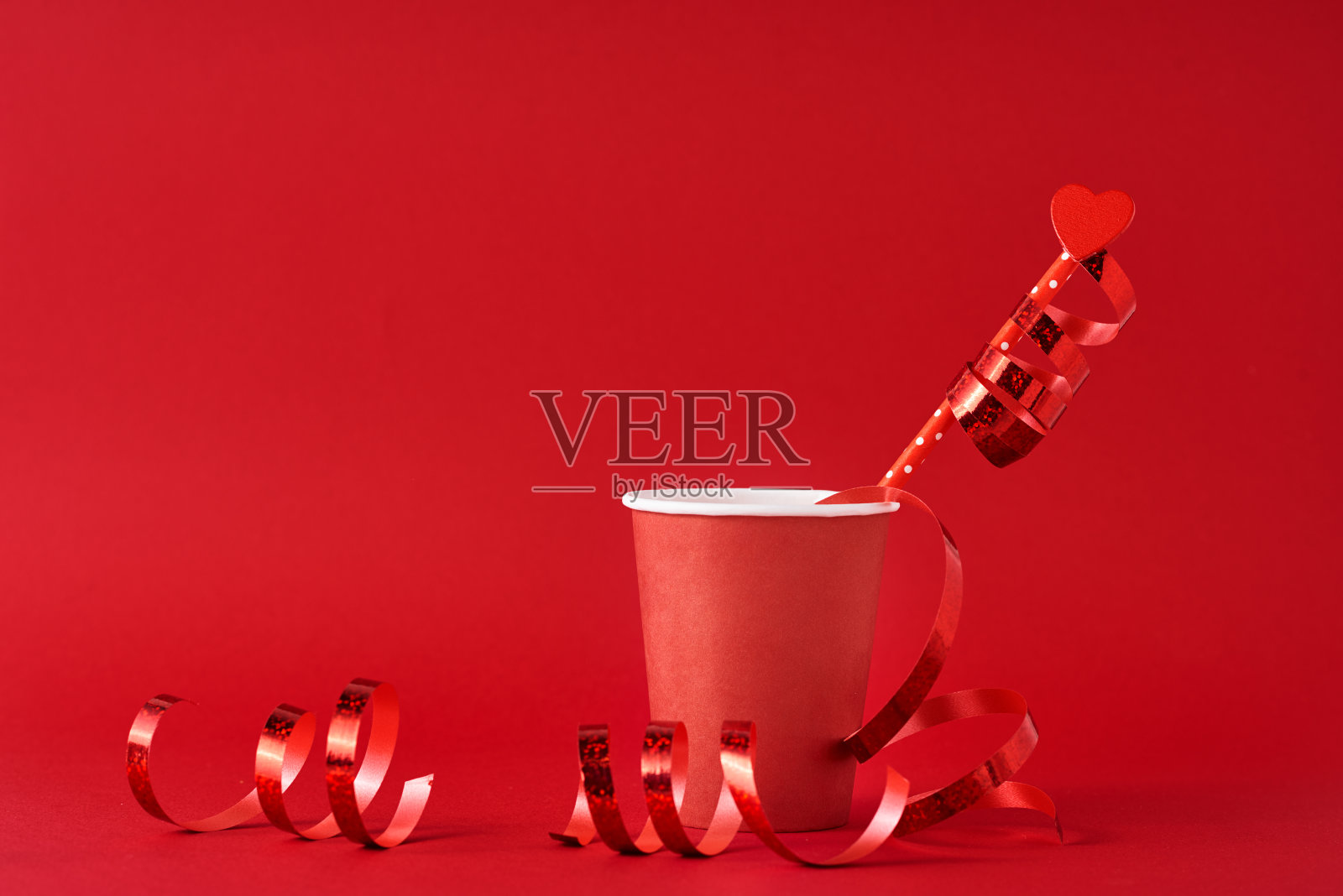 纸咖啡杯，稻草上有木心，红色背景上有节日彩带。情人节的概念照片摄影图片