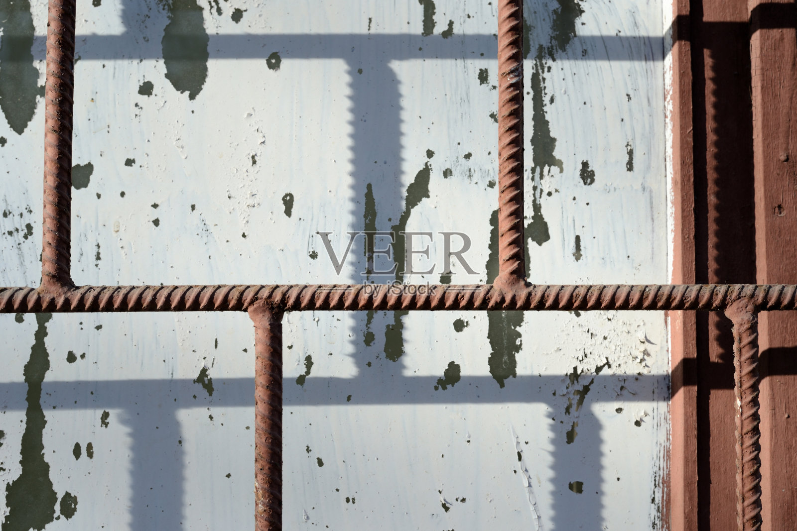 在阳光明媚的日子里，生锈的棕色铁条后面，漆着白漆的旧窗户。抽象的背景照片摄影图片