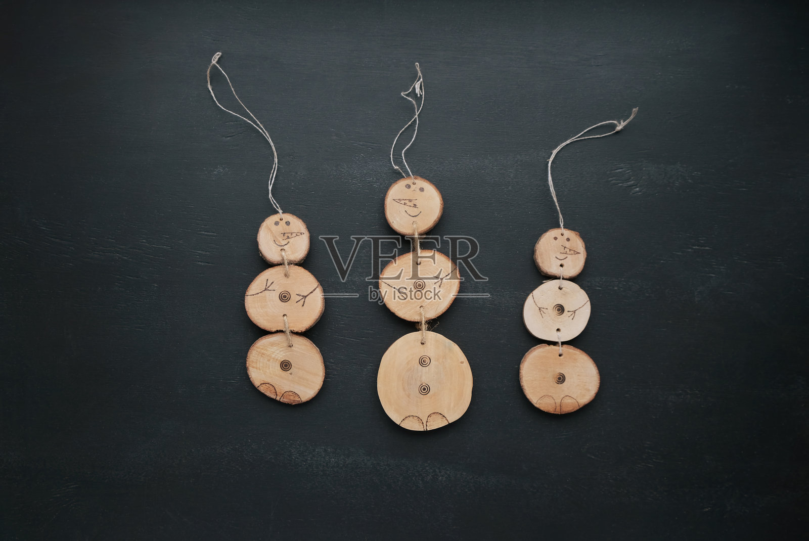 黑板背景上三个手工制作的木制雪人。天然工艺圣诞装饰。极简风格的圣诞卡。平放或俯视图。照片摄影图片