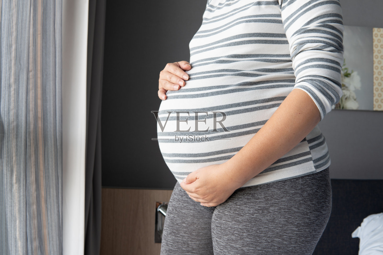 穿着蓝色裙子的孕妇把肚子放在白色的背景上。近距离的快乐怀孕的手触摸腹部健康的概念。母亲们站在医院里等待分娩。照片摄影图片