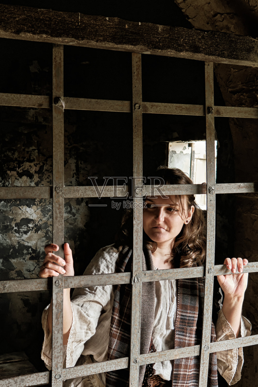 身穿18-19世纪复古连衣裙的年轻女子看着监狱牢房的栏杆照片摄影图片