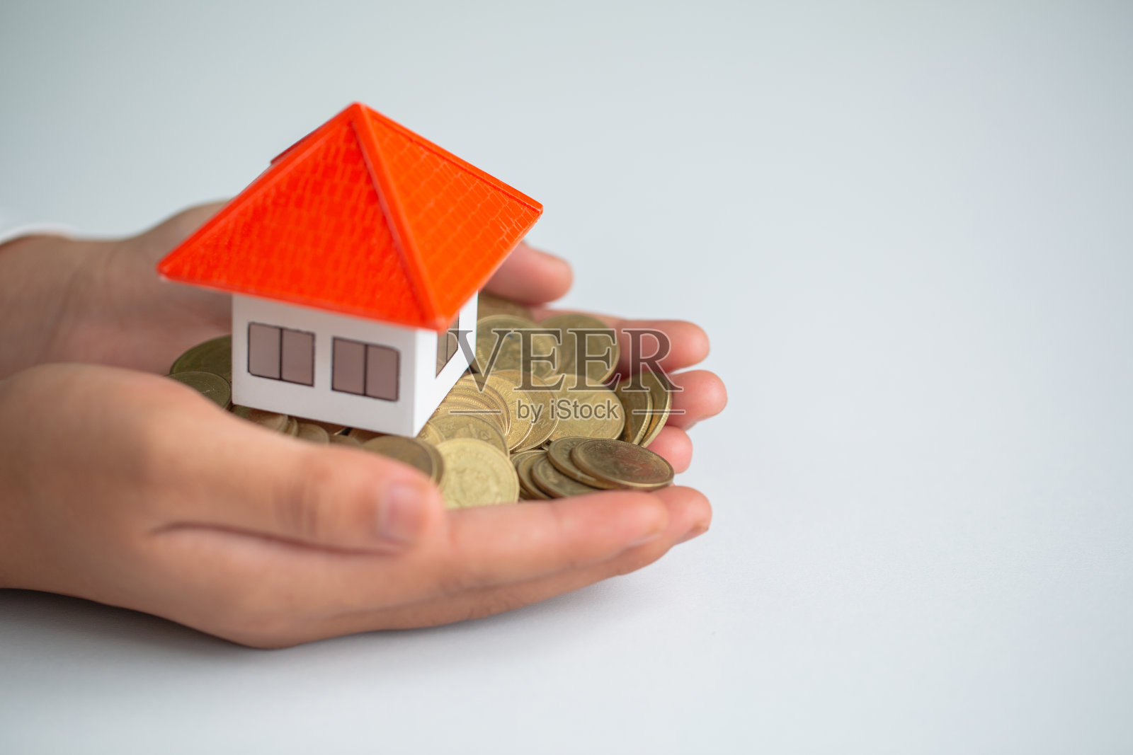 一个商人手里有一座橙色的房子和一枚硬币。省钱的主意，买房子和抵押，房地产和投资买房子。照片摄影图片