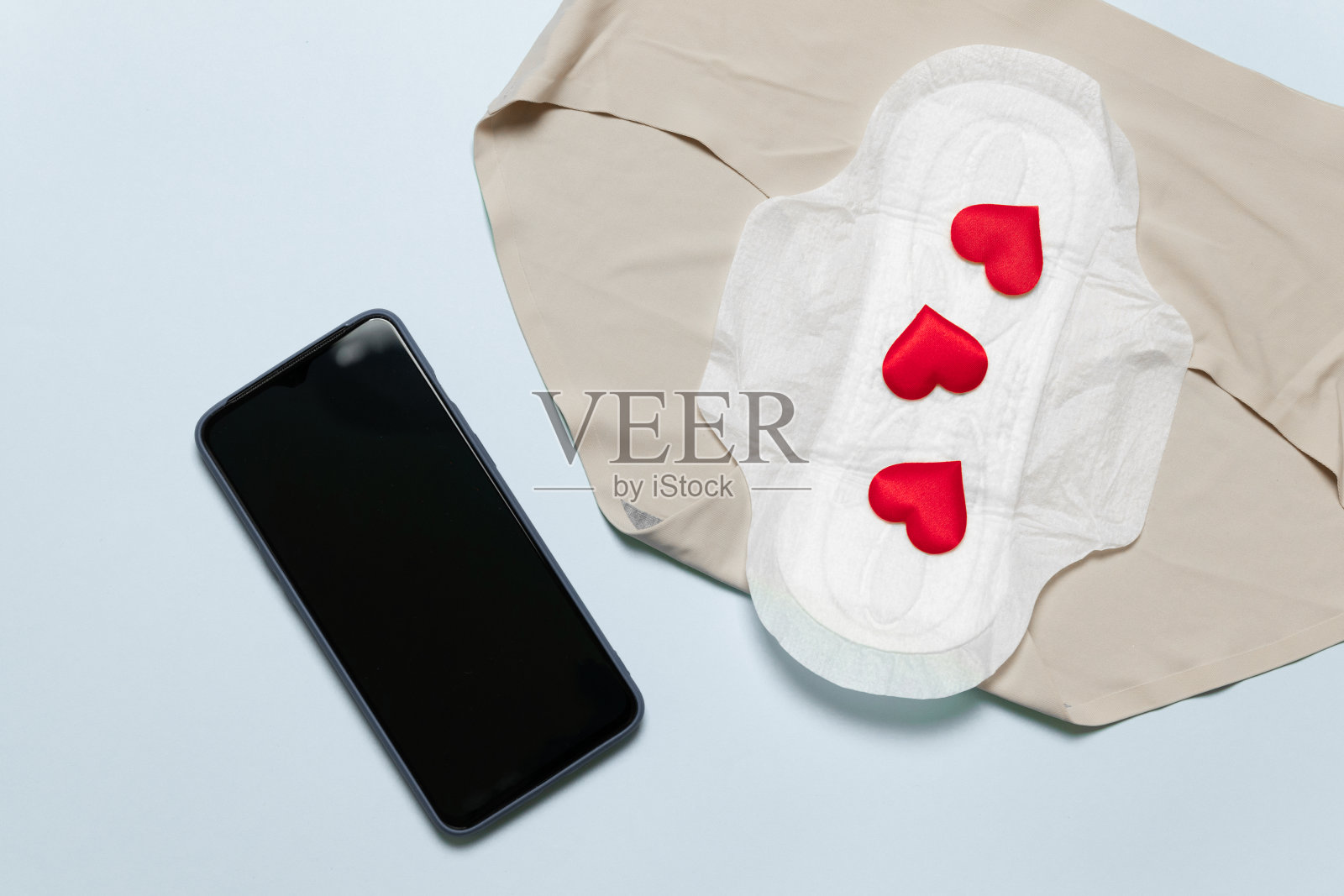 月经周期的概念。细长的棉质月经垫，红色爱的形状如血滴，智能手机在蓝色的背景。照片摄影图片