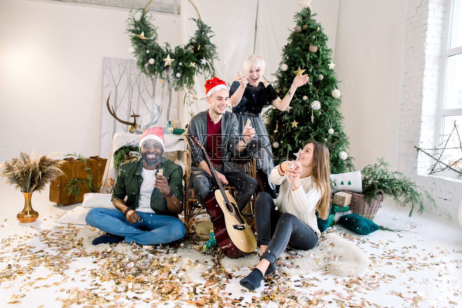 一群微笑的国际朋友与五彩纸屑飘动的乐趣。人们坐在家里的圣诞树和装饰品前照片摄影图片