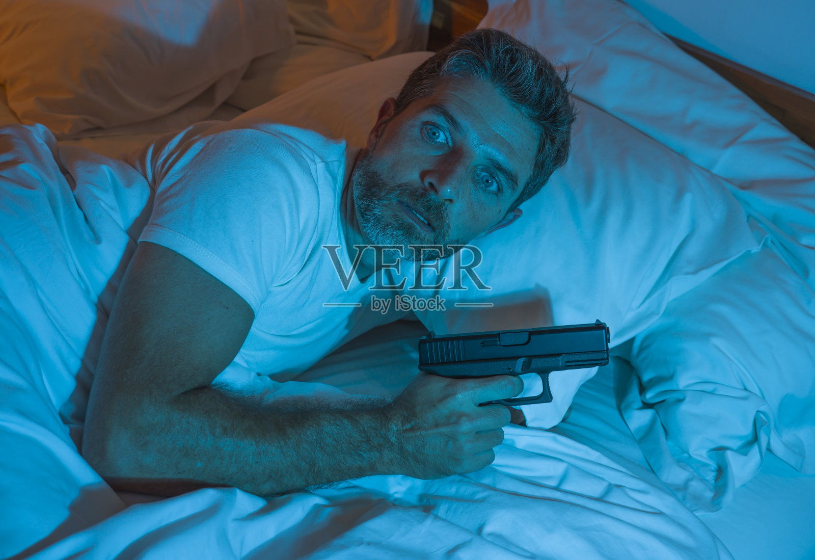 夜晚急躁的肖像，年轻的压力和偏执的美国人躺在床上不能睡觉，拿着枪看着周围害怕的感觉受到威胁，遭受偏执的自我保护概念照片摄影图片
