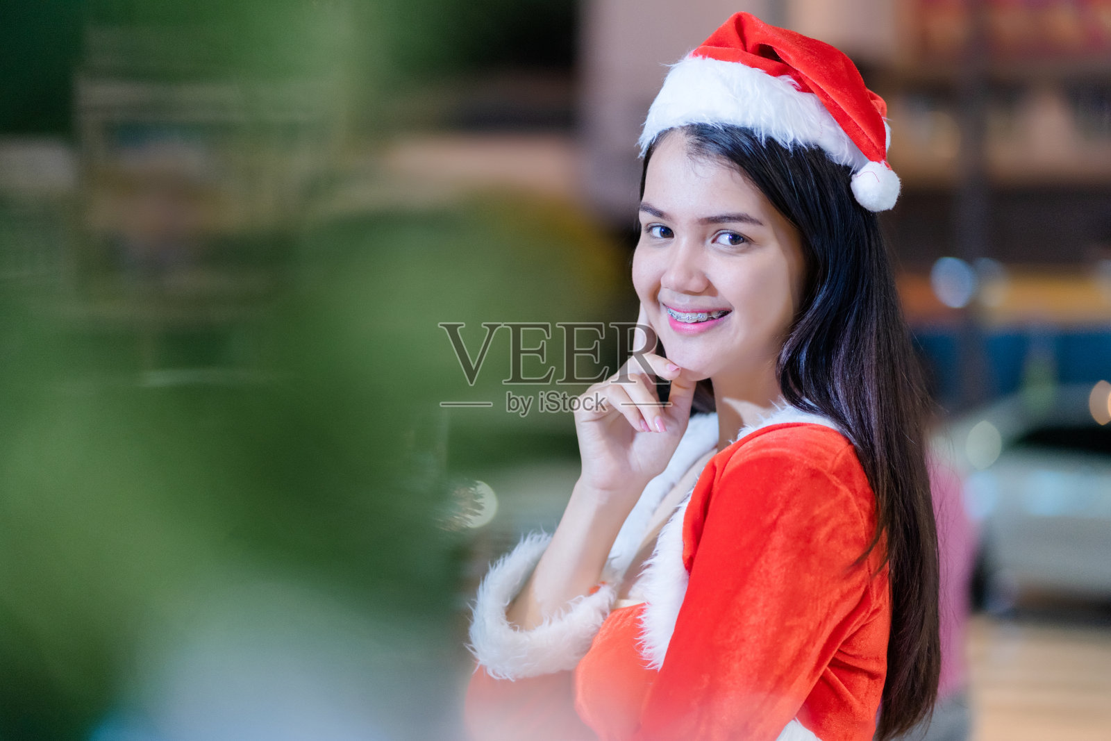 穿着圣诞老人服装，在散景灯光背景下赠送圣诞新年礼物的快乐亚洲女性肖像照片摄影图片