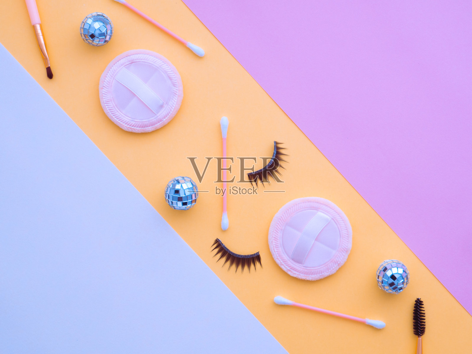 淡蓝色、白色、粉色、黄色粉彩纸、几何平面画背景，上面有化妆工具、圣诞球、粉扑、棉签、假睫毛等。副本的空间。照片摄影图片