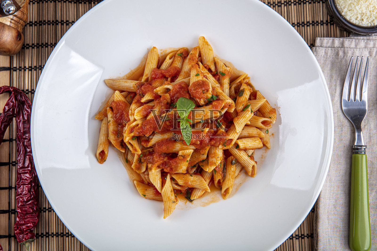 带有辣椒酱的通心粉。经典的意大利番茄通心粉配罗勒和新鲜磨碎的羊乳干酪放在质朴的木桌上。照片摄影图片