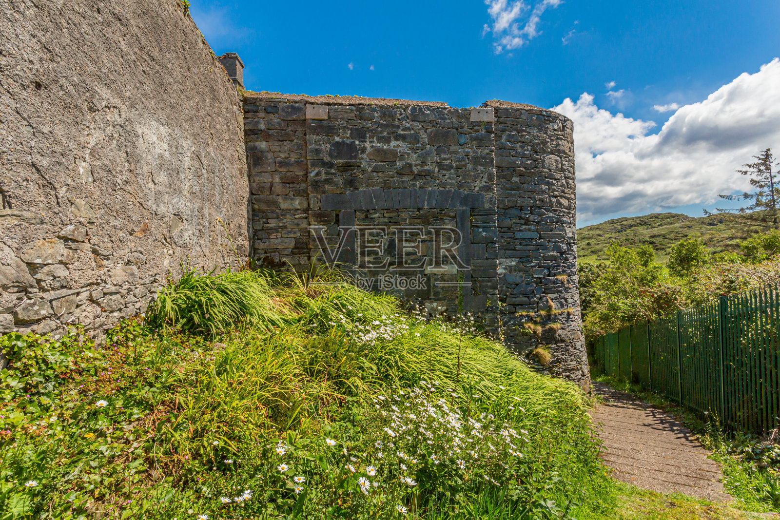 旧拘囿监狱的石墙，旁边是一条小路，金属栅栏的背景是群山照片摄影图片
