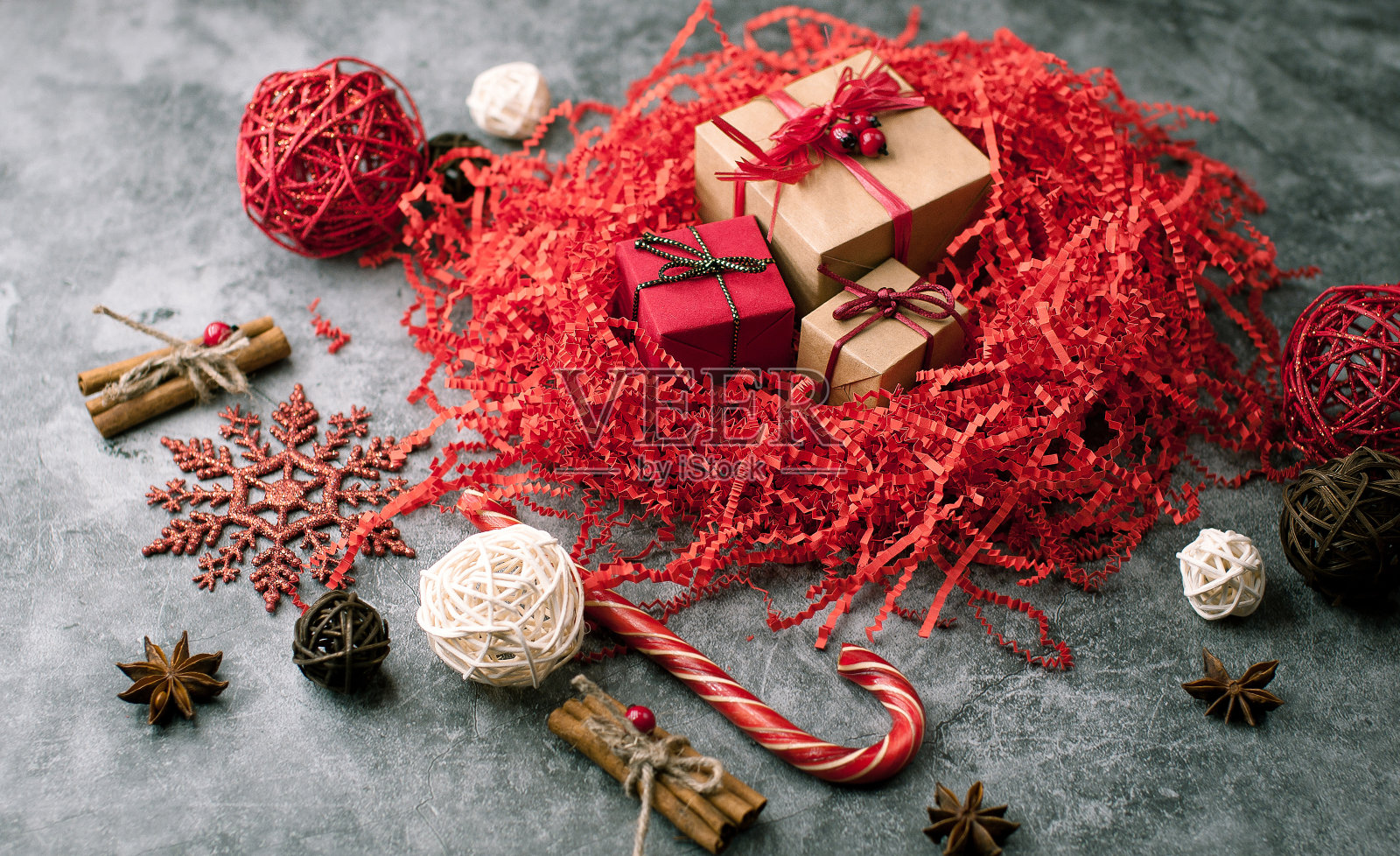 圣诞暗色陈年背景下的水泥桌子上装饰着红色的装饰品，包裹着丝带、礼物、雪花、藤球和红色的瓦楞剪纸照片摄影图片
