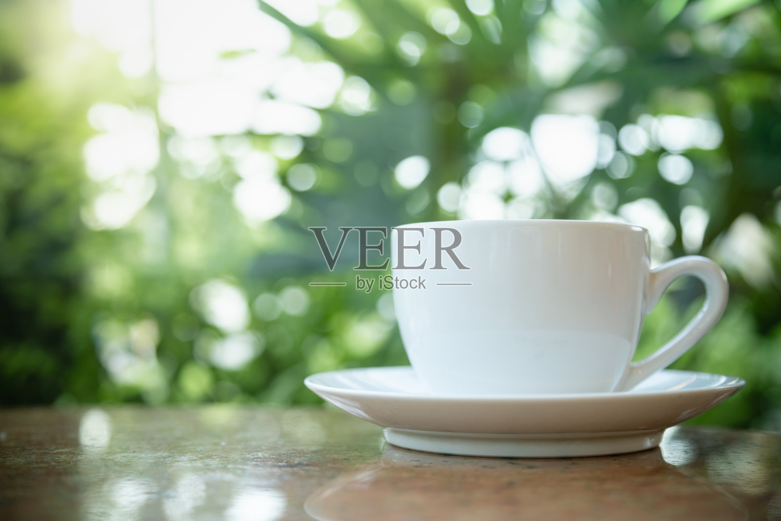 木桌上热咖啡杯碟特写，绿色树叶背景照片摄影图片