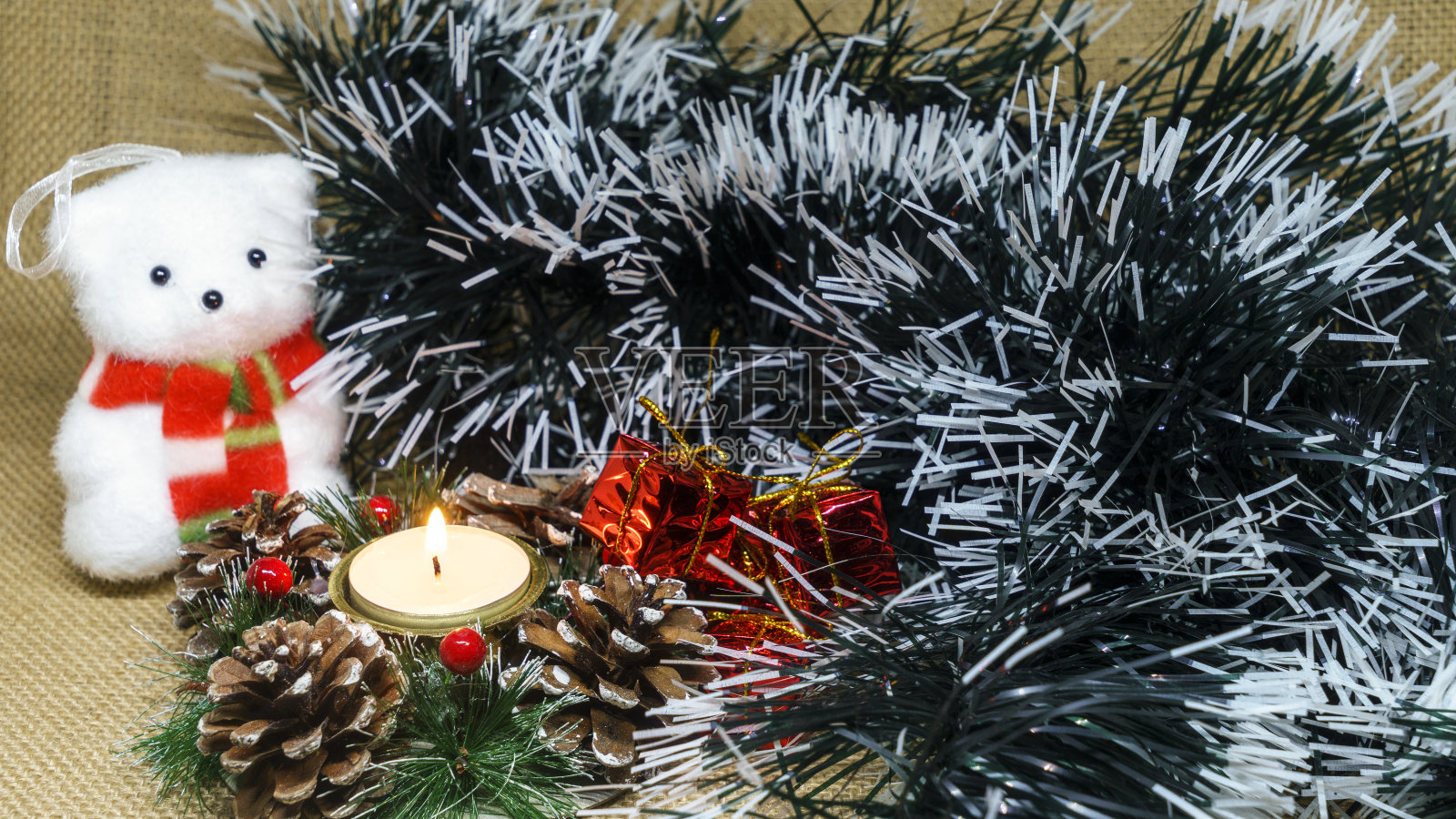 圣诞蜡烛白色泰迪熊，礼物和绿色金属箔在麻袋背景。冬天的概念照片摄影图片