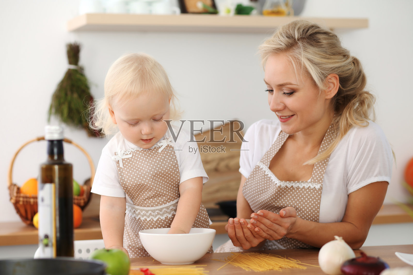 快乐的妈妈和小女儿在厨房做饭。花时间在一起，家庭乐趣的概念照片摄影图片