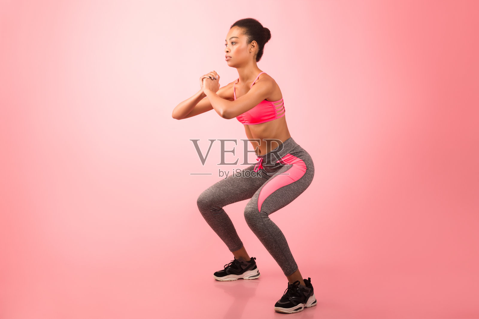 非洲女孩做深蹲练习在粉红色的背景照片摄影图片