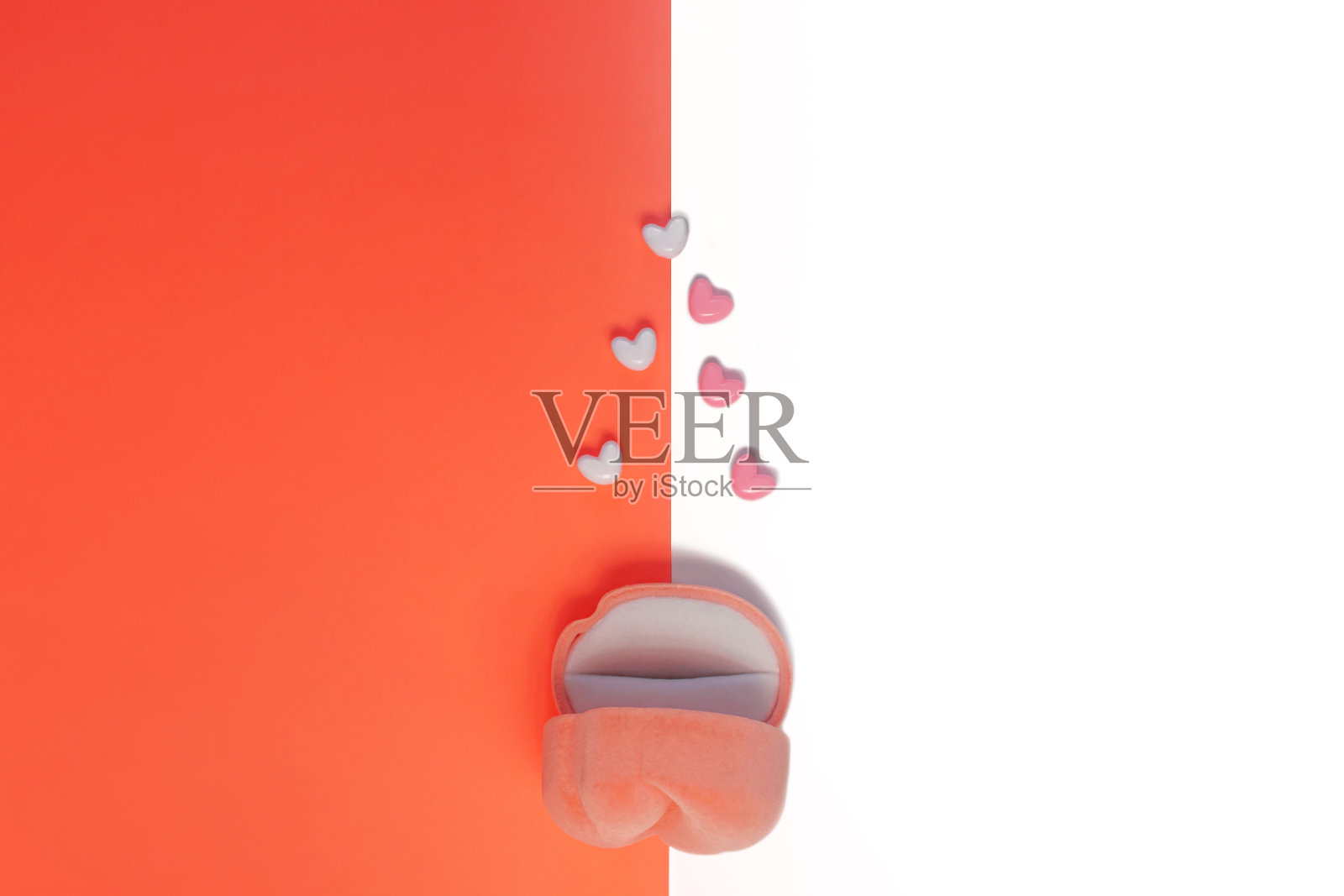 白色和珊瑚橙色背景上的粉色天鹅绒戒指盒，带有心形图案。情人节婚礼求婚珠宝袋照片摄影图片